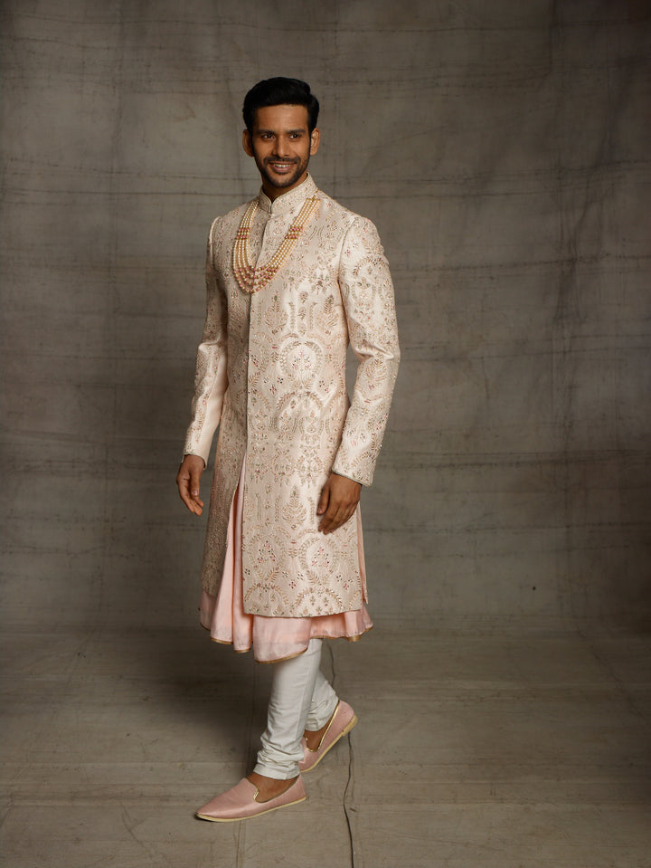 Powder peach sherwani with resham work and mirror highlights.