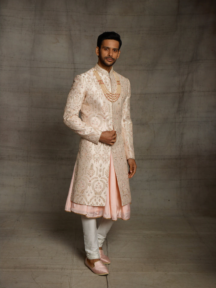 Powder peach sherwani with resham work and mirror highlights.